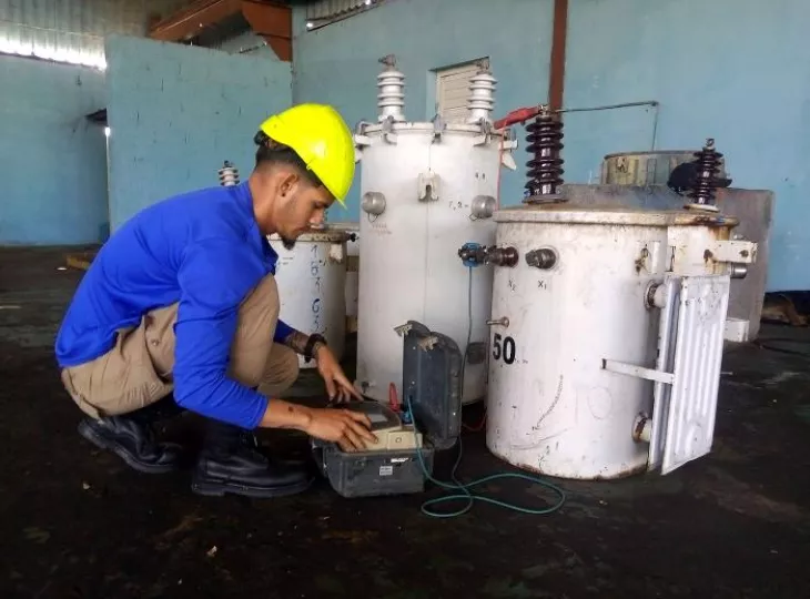 Trabajador en un taller eléctrico realizando labores de mantenimiento a un transformador.