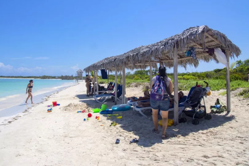 Vista panorámica de una playa cubana con estructuras de sombra y vegetación en el entorno.
