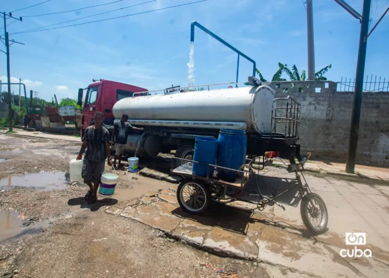 Personas llenando recipientes con agua en La Habana junto a una pipa de servicio.