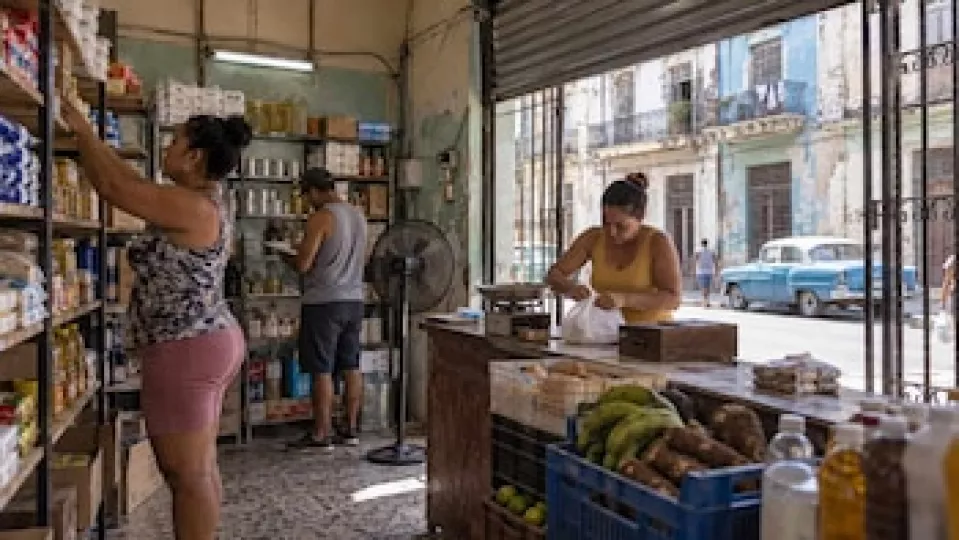 Mostrador de un mercado de barrio con estantes parcialmente abastecidos y pizarra de precios en Cuba.